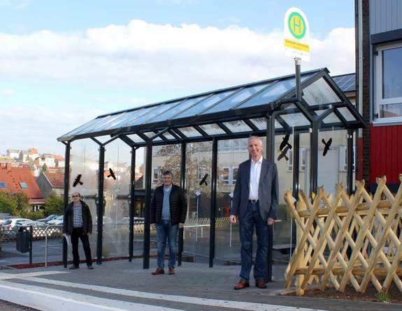 Drei Männer stehen an der neuen Bushaltestelle der Lasbachschule