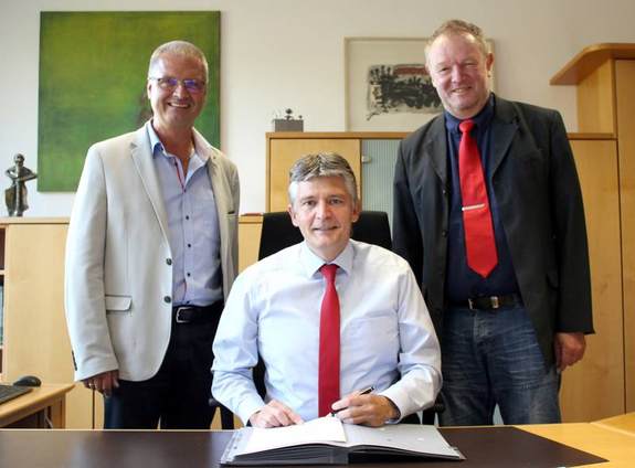 Bürgermeister Lutz Maurer, sitzend an seinem Schreibtisch im Büro, links davon steht Thomas Lermen, Gaswerk Illingen, rechts steht Patrick Weydmann, Bürgermeister Merchweiler